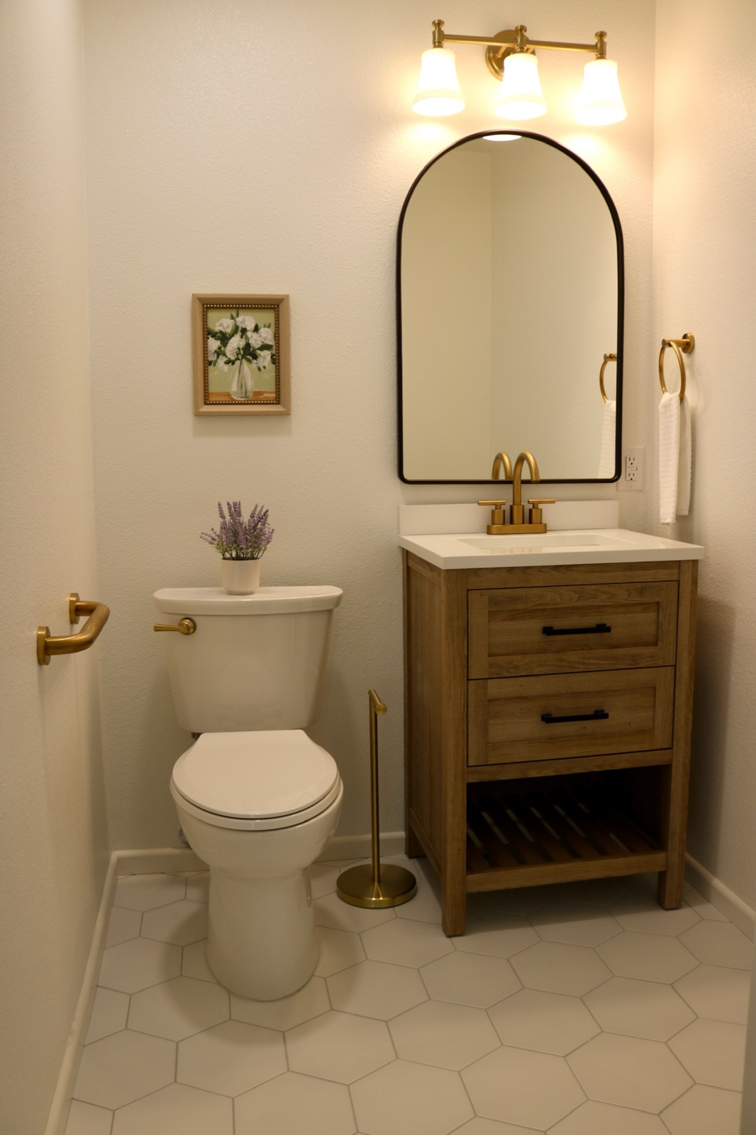 Private half bath with a wood vanity, arched mirror, and lit vanity fixture