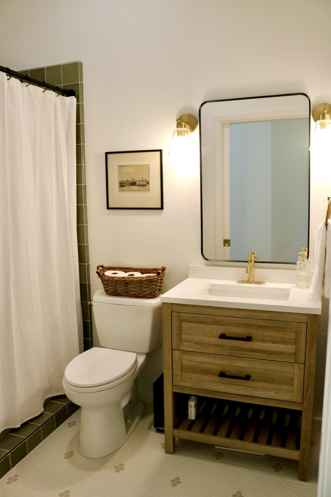 Private bath with a green-tiled shower, wood vanity, and lit wall sconce