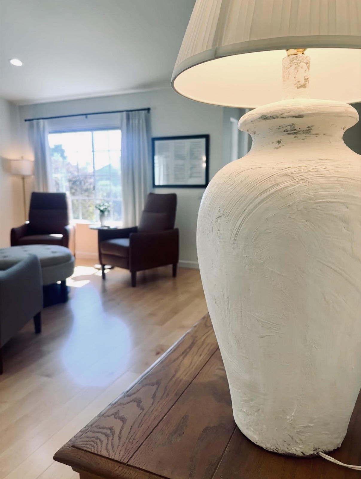 Textured white table lamp lit beside the living room seating and a bright window