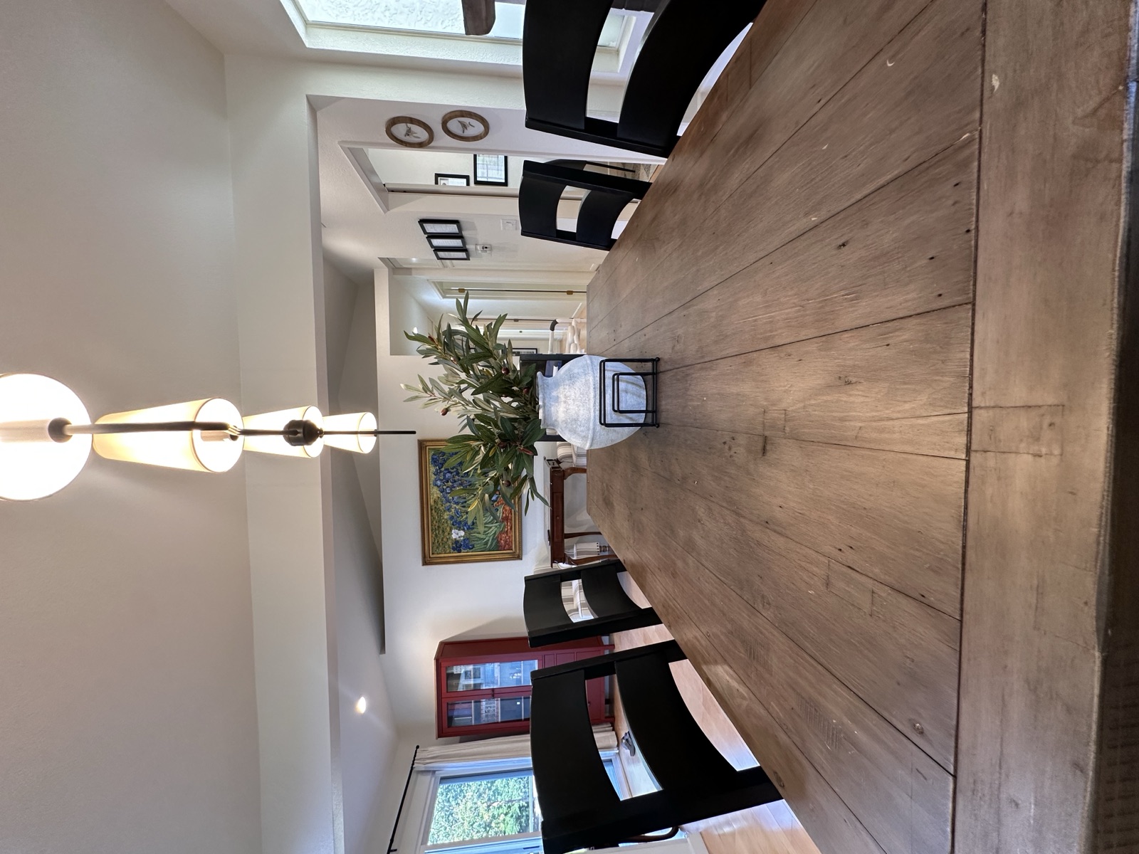 Long wood dining table with black chairs under a lit pendant light