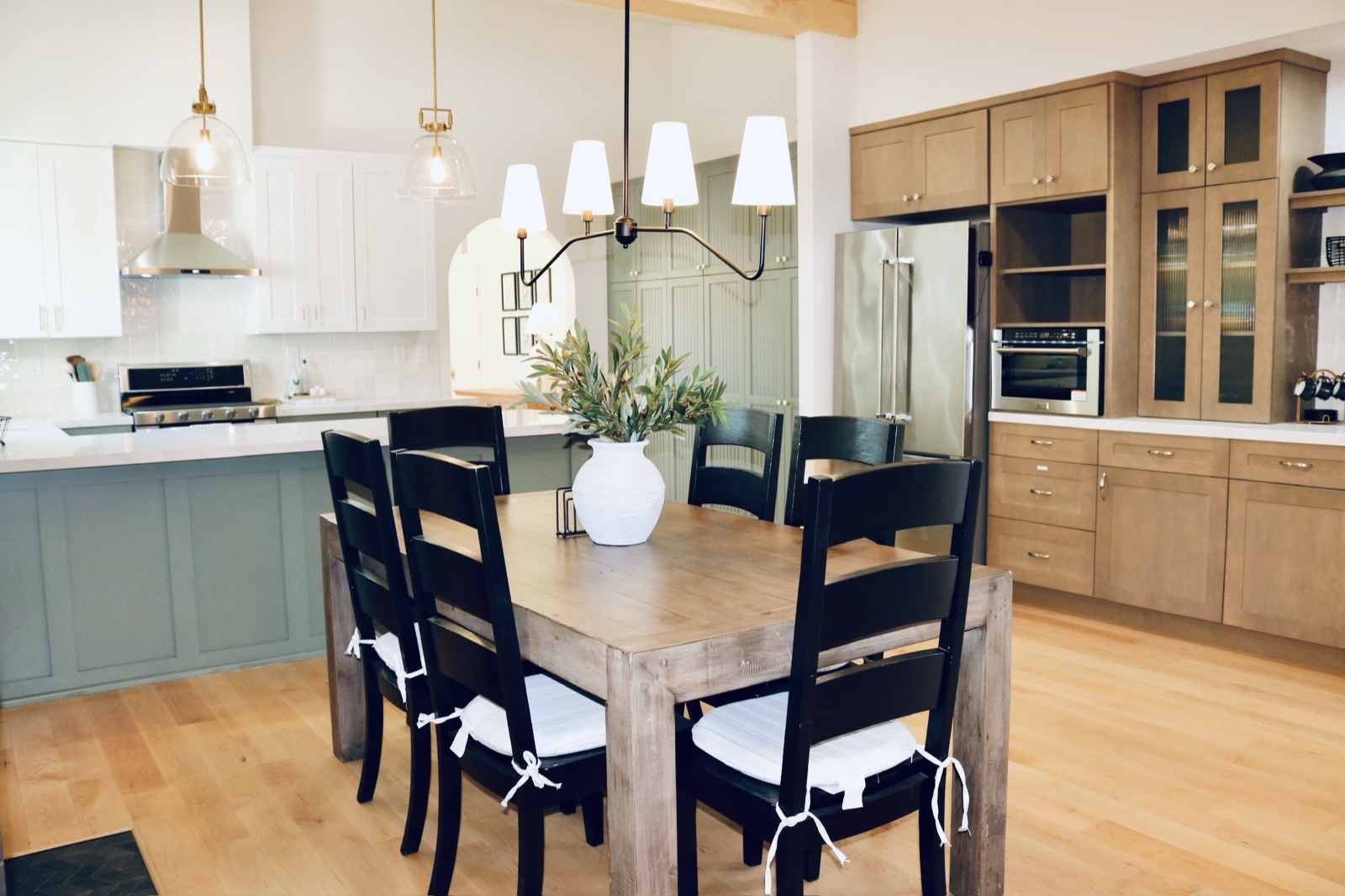 Family-style dining table open to the kitchen under a lit chandelier