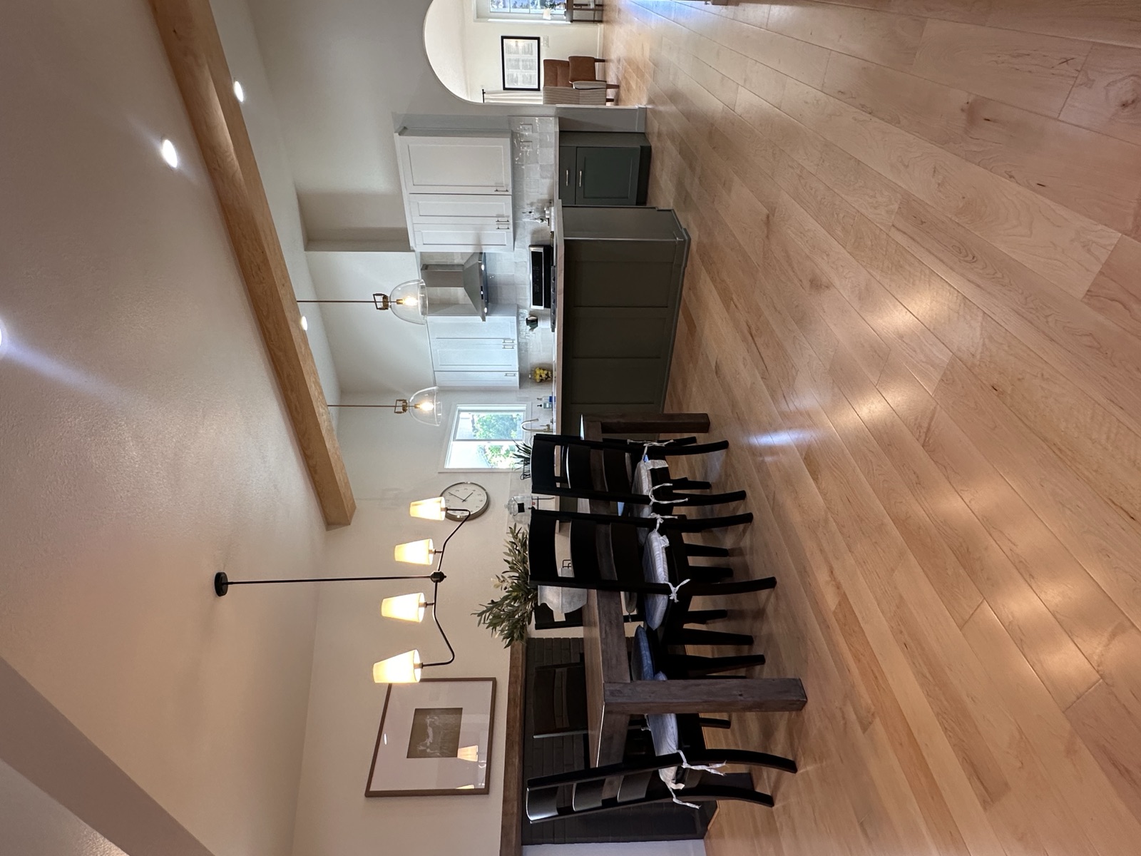 Dining table and kitchen island beneath pendant lighting on wide hardwood floors