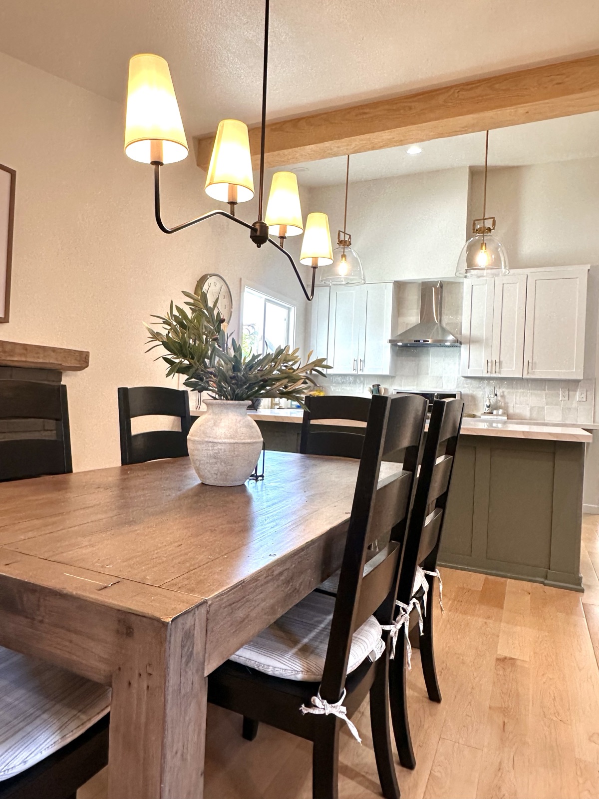 Dining table set beneath a lit chandelier with the kitchen beyond