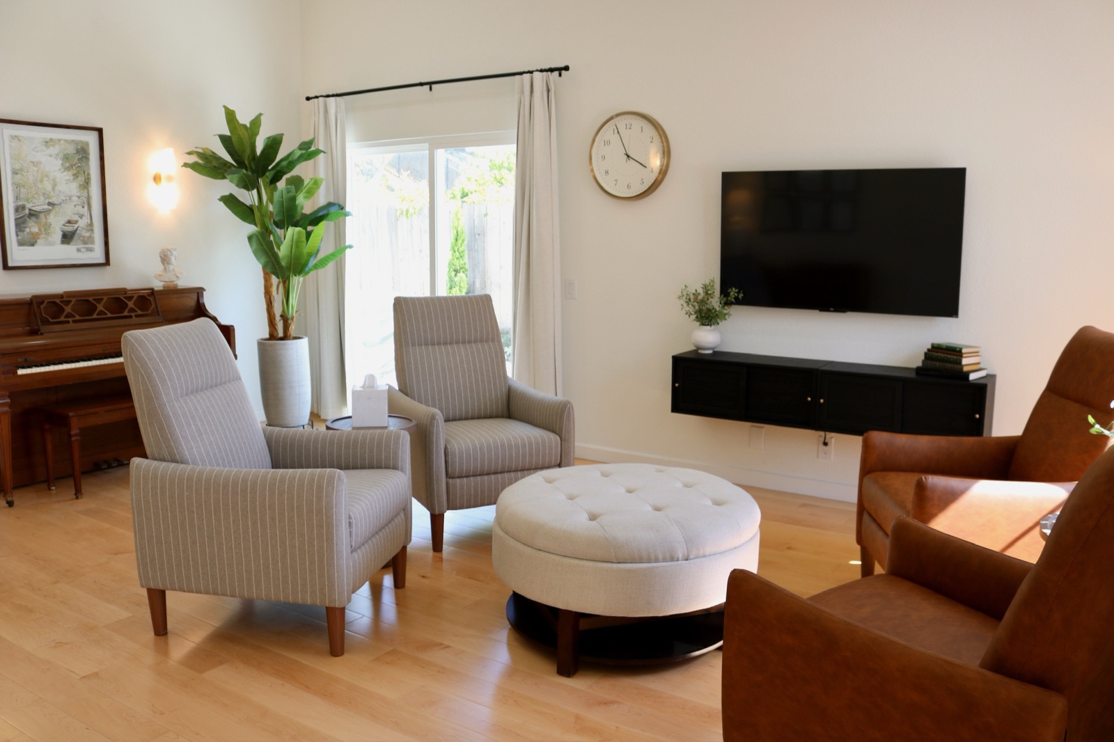 Living room seating arranged around a soft ottoman with a wall-mounted television