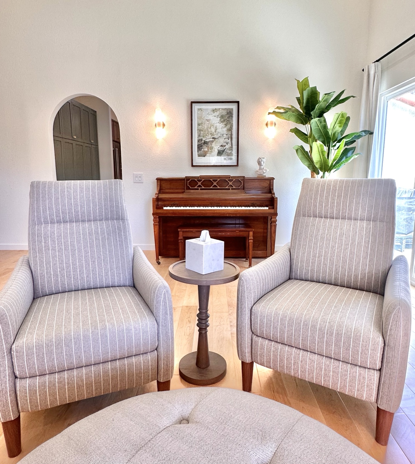 Two grey armchairs facing the piano beneath lit wall sconces