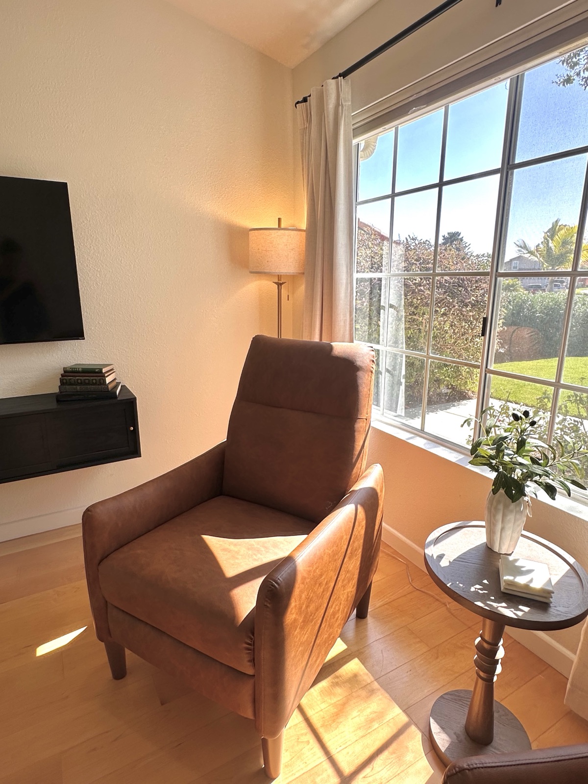 Leather reading recliner beside a sunny window with a lit floor lamp