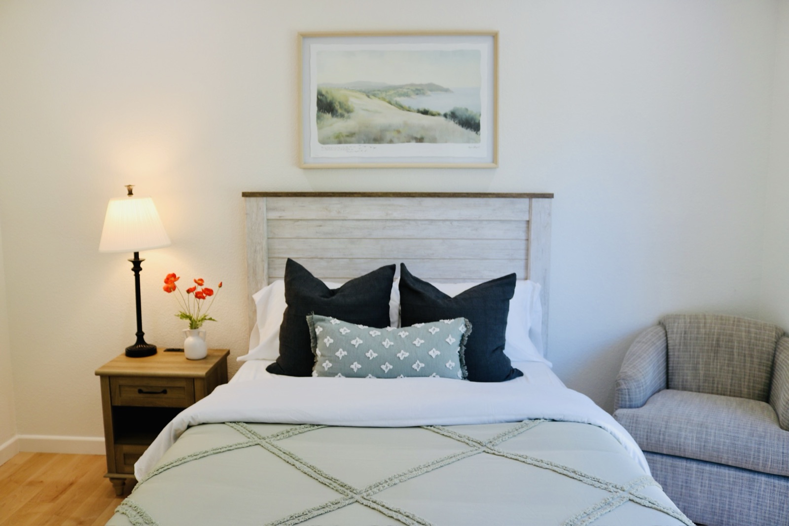Made bed with fresh linens, a lit bedside lamp, and flowers in a private room