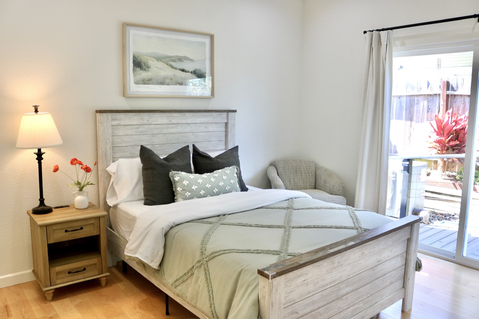 Private room with a lit bedside lamp and sliding door to a planted patio